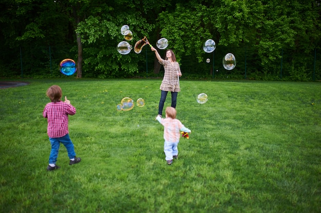 Mom and children playing soap bubbles on the green lawn in the park.