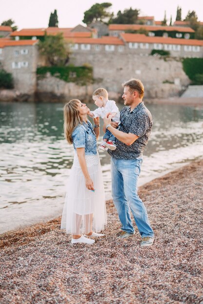 Mom and dad are holding their little son in their arms by the sea against the backdrop of the Sveti