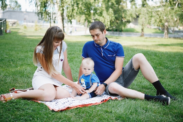 Mom, dad and blond son are sitting on a green lawn in the summer