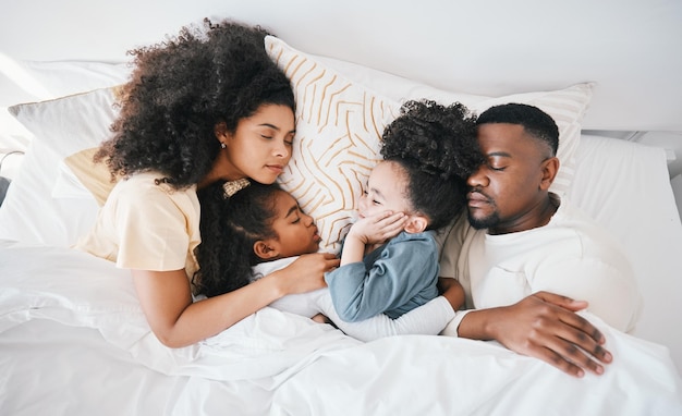 Mom dad and kids in bed sleeping and top view for care hug and relax together on holiday in family home Mother father and tired children for bonding love or rest in bedroom for fatigue in house