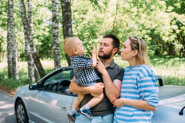 Mom dad and little son in a convertible car summer family road trip to nature