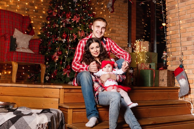 Mom and dad pose with their charming little daughter in decorated christmas studio. New Year photo session.