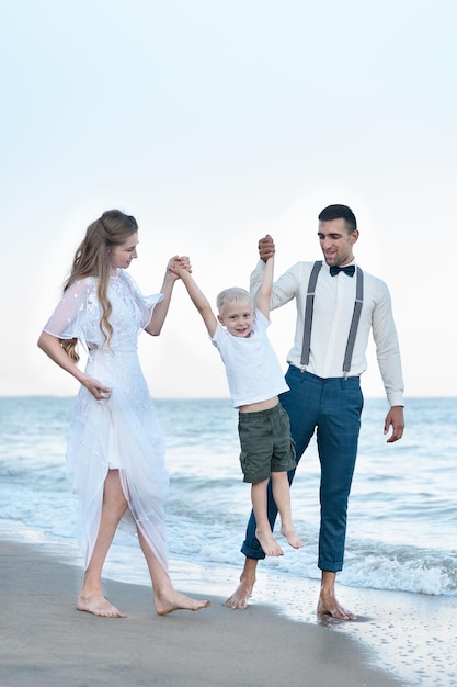 Mom and dad raise the child's hands Young family walks on the beach Happy parenthood and childhood Vertical frame