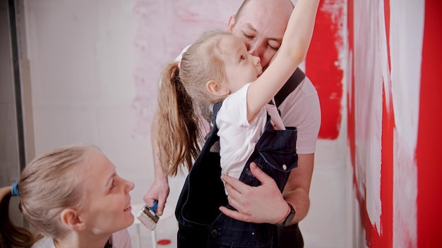 Mom and dad teaching his little daughter how to paint walls  raise her higher