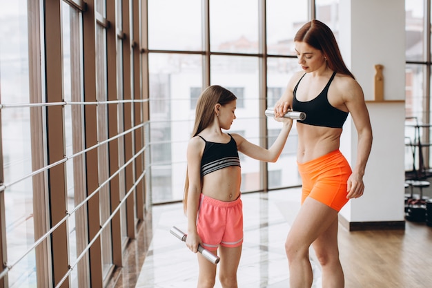 Mom and Daughter are doing exercises. Family in a gym. Little girl with strong mother are training with dumbbells