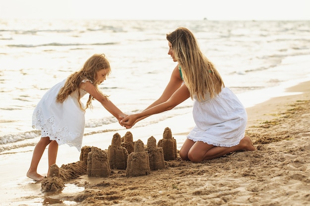 Mom and daughter build sand castles on the beach on a sunny summer day