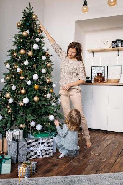 Mom and daughter decorate the Christmas tree indoors.