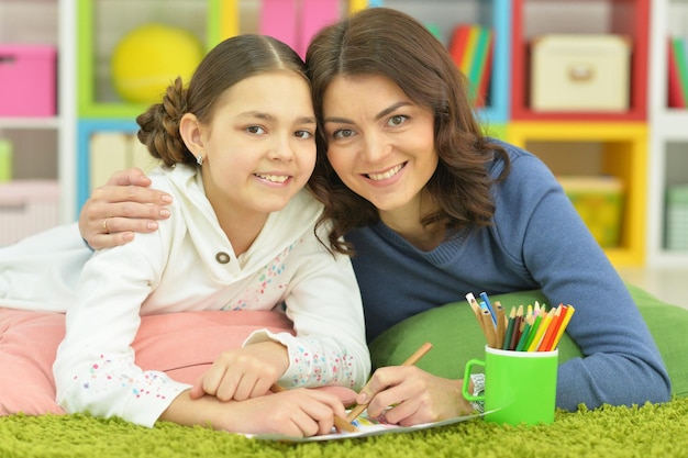 Mom and daughter have fun drawing lying on the carpet