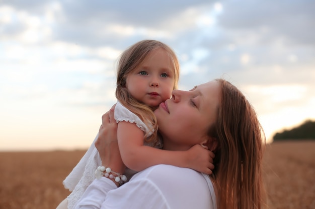 mom and daughter hug and kiss each other on the background of the sky and wheat