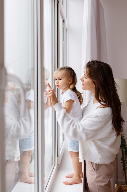 Mom and daughter look out the window of the house