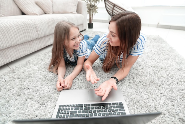 Mom and daughter lying on the carpet and using a laptoppeople and technology