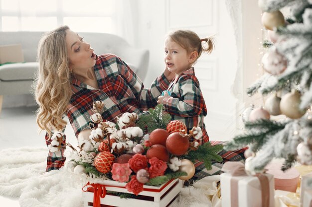 Mom and daughter in plaid pajamas sitting near Christmas tree