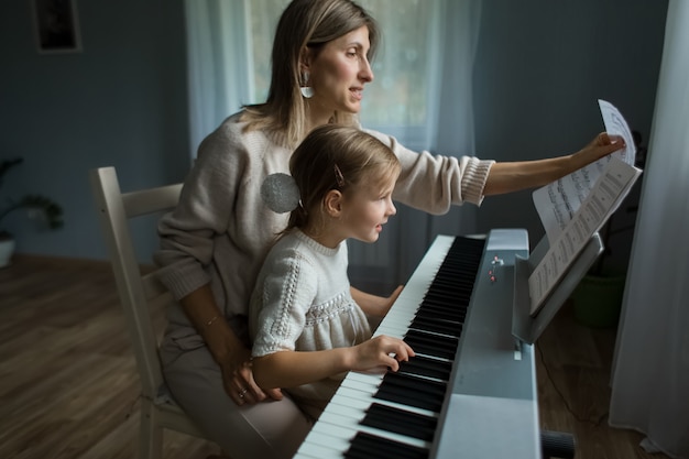 Mom and daughter play the synthesizer in the house. Learning on the synthesizer at home. High quality.