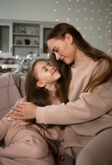 Mom and daughter in sweatshirts are sitting on the couch and hugging