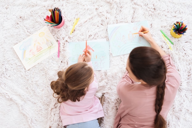 Photo mom and daughter together draw on paper with pencils.