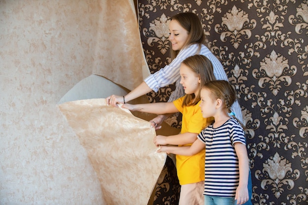 Mom and daughters together remove old wallpaper from the walls