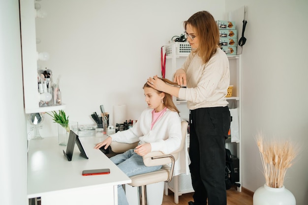 mom does her daughter hair a teenager uses a tablet