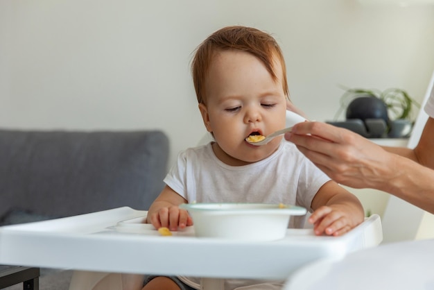 Mom feeds Little child sitting at the childrens table at home