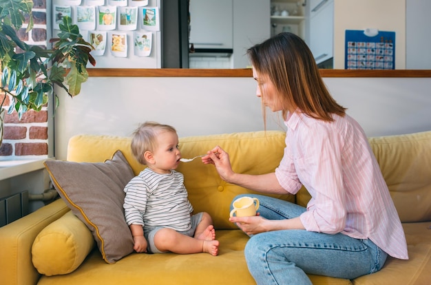 Mom feeds a small child at home with yogurt from a spoon family concept