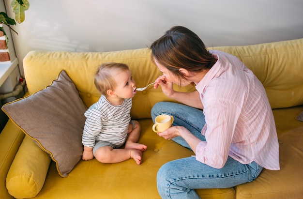 Mom feeds a small child at home with yogurt from a spoon Family concept