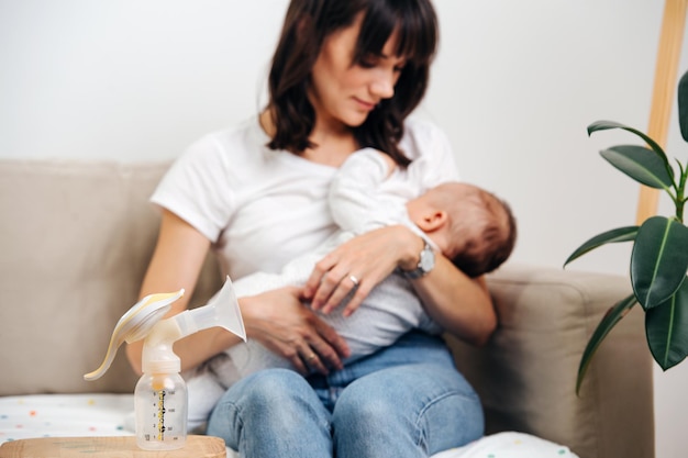 Mom gently looks at the baby and breastfeeds, next to the table is a breast pump for milk.