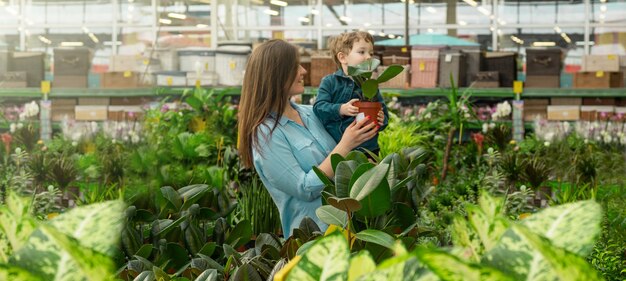 Mom and her baby boy in a plants shop choose plants. Gardening In Greenhouse. Botanical garden, flower farming, horticultural industry concept