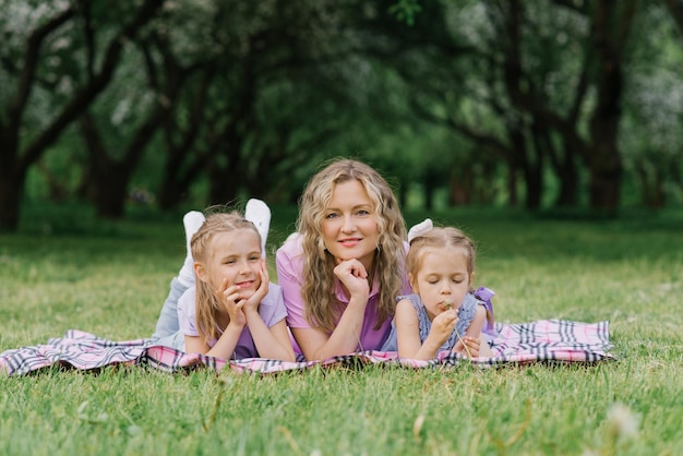 Mom and her daughters are lying on the blanket in a summer park The family has fun outdoors