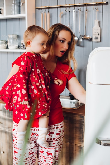 Mom holding by hand little daughter , showing and looking inside refrigerator.