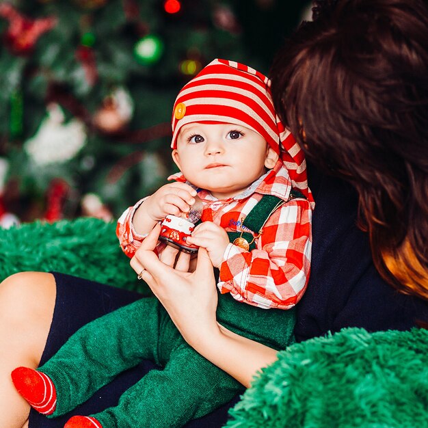 Mom holds on her knees little boy in red suit 