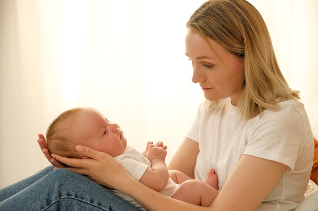 Mom holds a newborn baby in her arms in the background the sun shines from the window