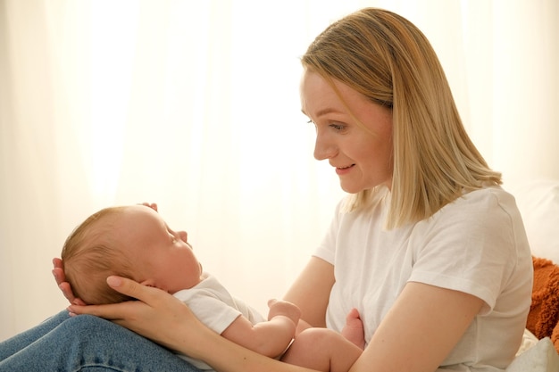 Mom holds a newborn baby in her arms in the background the sun shines from the window