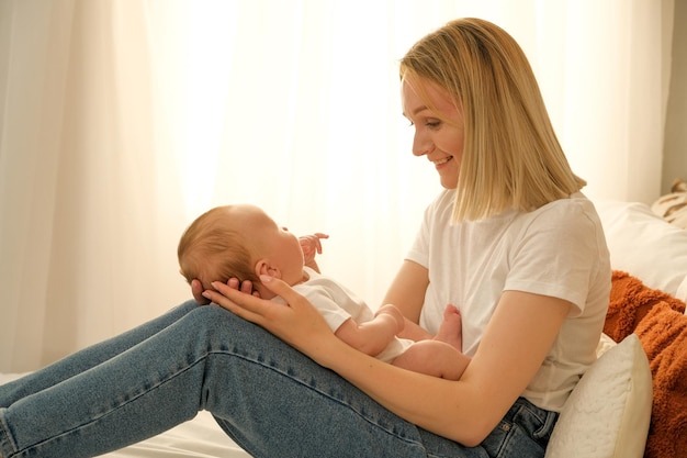 Mom holds a newborn baby in her arms in the background the sun shines from the window