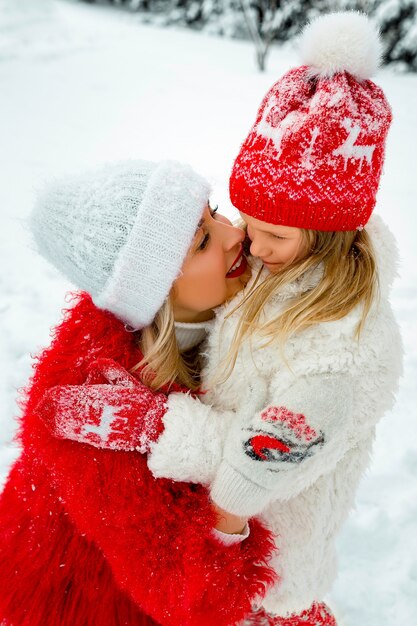 Mom hugs her daughter . family portrait against the backdrop of a snowy yard. family look.