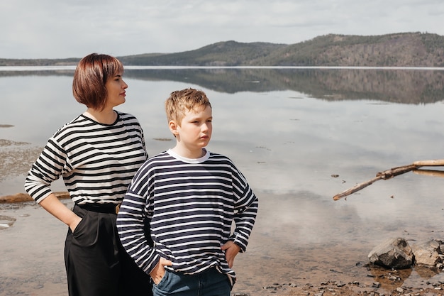 Mom hugs her son on the riverbank. A beautiful, modern mother with a happy son in striped vests.