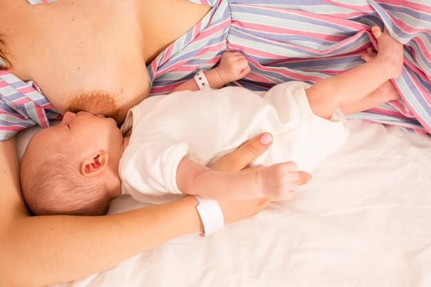 The mom is breastfeeding her newborn baby on the bed