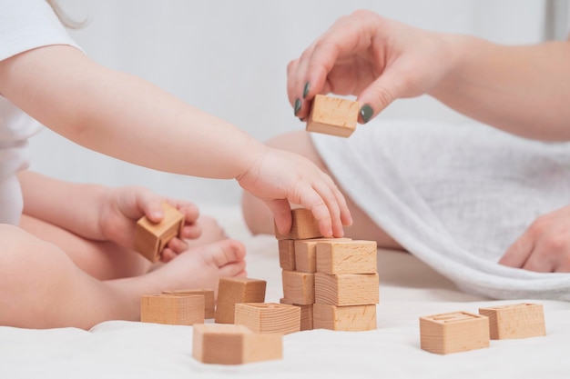 Mom is playing with a child building a house out of wooden ecofriendly cubes closeup The concept of early child development through games Cozy homely atmosphere Mothers Day Childs Day