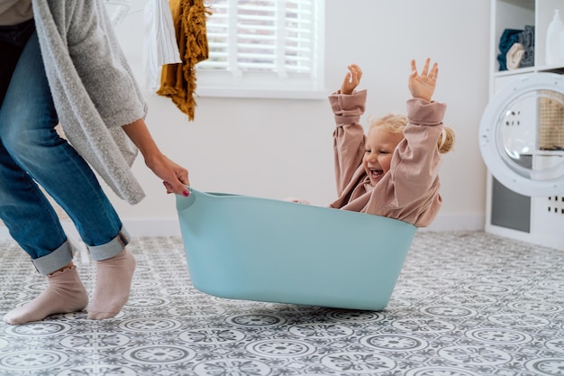 Mom is playing with daughter who is sitting in laundry bowl little girl wants to spend time