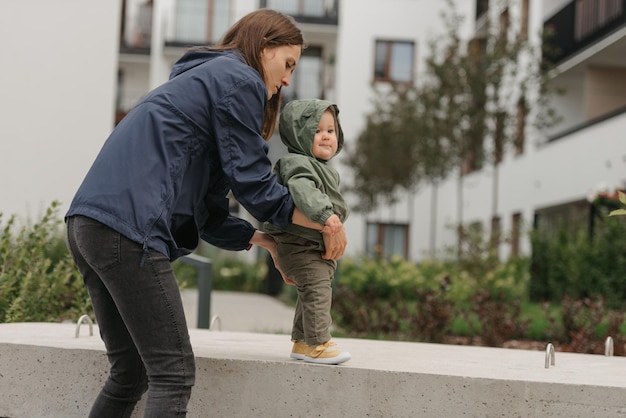 A mom is teaching her female toddler how to do steps in the street at noon