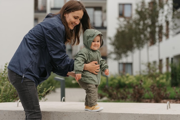 A mom is teaching her female toddler how to do steps in the street at noon