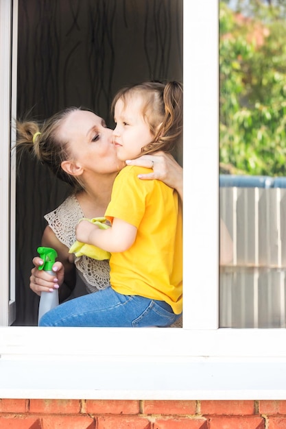 mom kisses her little daughter while cleaning the house, she washes the windows