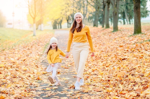 Mom in a knitted hat with her daughter walking looking into the lens in the autumn park with a wide smile