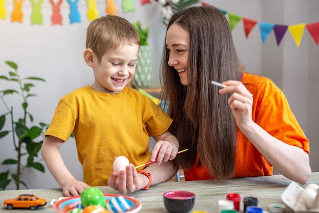 Mom and little child together are coloring eggs and having fun Concept of family preparation for Easter festive spring mood