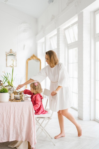 Mom and little daughter are sitting at a festive Easter table in the living room