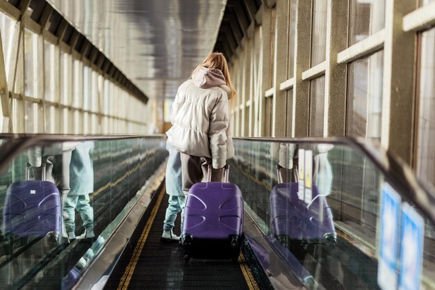 Photo mom and little daughter go up the escalator to the building of the station or airport