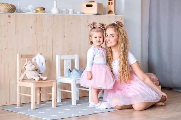 Mom and little daughter in pink skirts cuddle at home