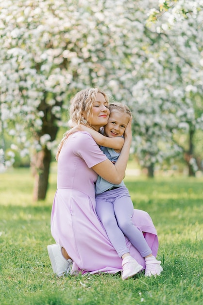 Mom and little daughter walk through the blooming spring garden and hug