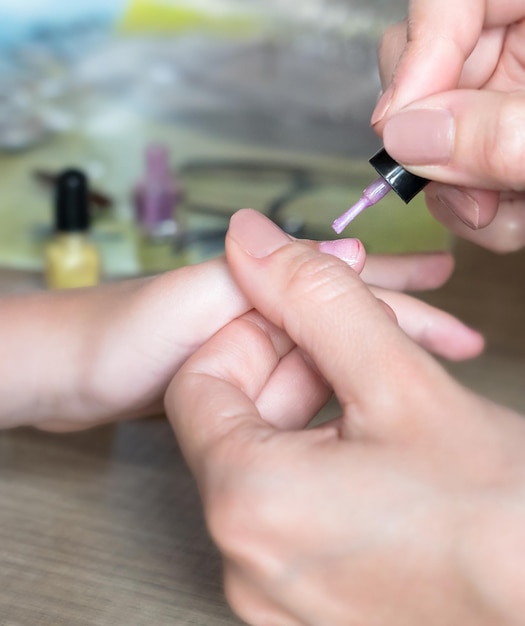 Mom paints daughters nails on hands with pink nail polish on table