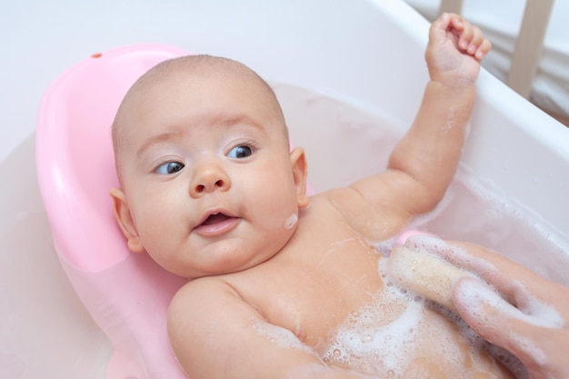 Mom's hand with a sponge washes the baby in the bathroom