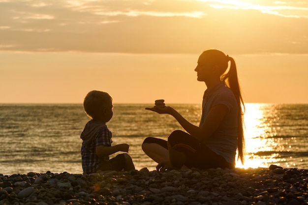 Mom and son are playing on the beach at sunset