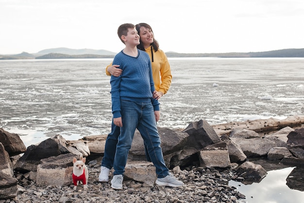 Mom and son are standing on the river bank with a Chihuahua dog. Nature and recreation.